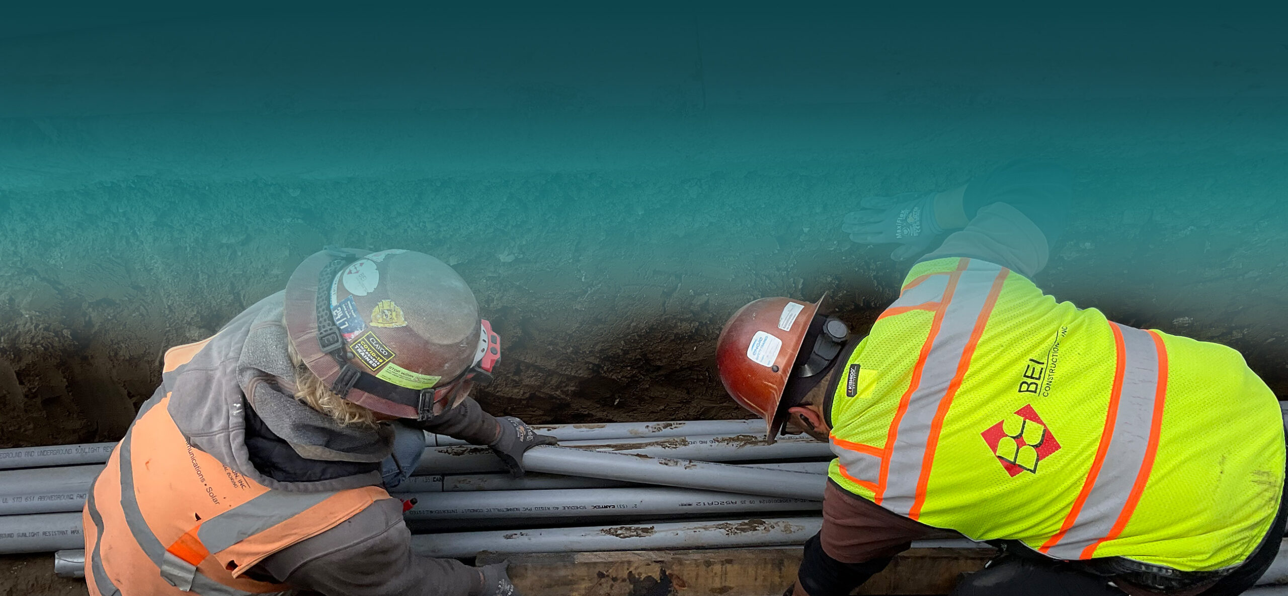 Two workers equipped with protective gear, including helmets, gloves, and reflective vests, are diligently working underground. 