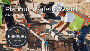 construction worker wearing a white hard hat, safety vest, gloves, and jeans smooths freshly poured concrete on a job site. Text over the image reads "Platinum Safety Award – 2025 Winner" alongside the Highwire 2025 Platinum Safety Assessed Contractor badge (ID: 21093)